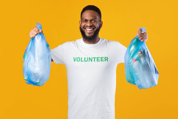 Black Volunteer Guy Holding Bags With Plastic Litter, Yellow Background - Фото, зображення