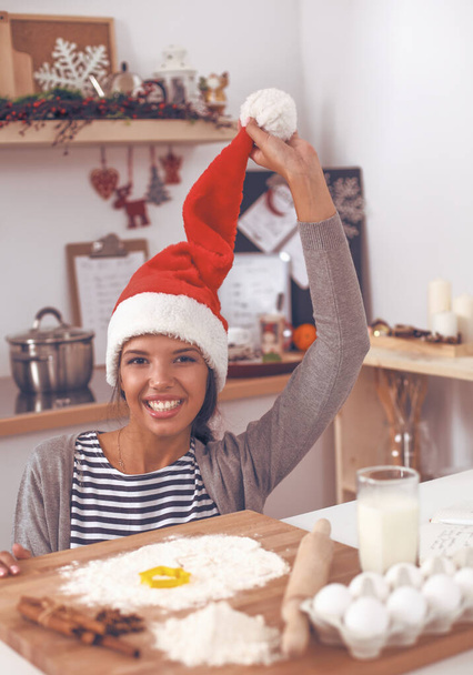 Woman in santa hat making christmas cookies in the kitchen - Fotó, kép