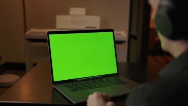Kaukasischer Mann mit Kopfhörer hört Musik hinter grünem Bildschirm-Laptop. - Filmmaterial, Video