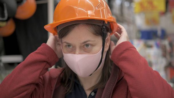 Γυναίκα σε αντι βακτηριακή μάσκα βάζει σε ένα κράνος κατασκευής - Φωτογραφία, εικόνα