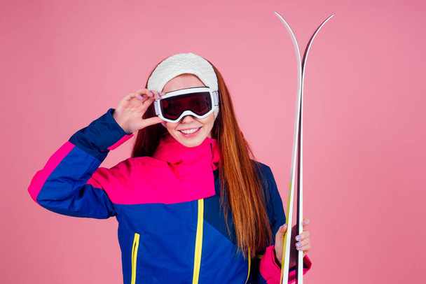 redhaired ginger young woman with skis posing in studio on pink background - Foto, Imagem
