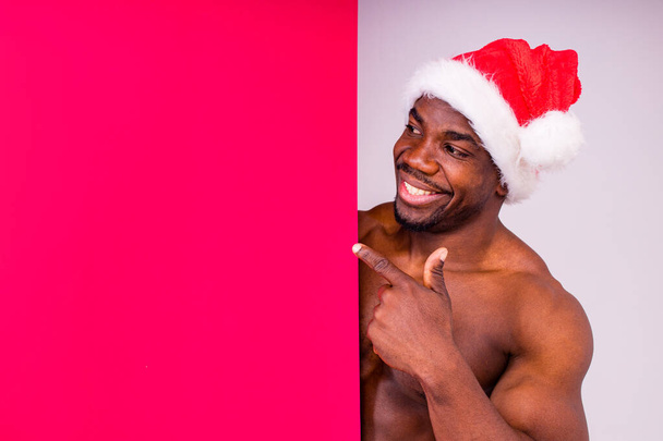 naked nude african american man holding gift box with white ribbon tie bow in red studio background - Foto, Imagen
