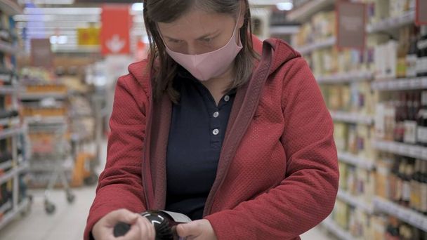 Pembe maskeli kadın dükkânda elinde şarap şişesi tutuyor. - Fotoğraf, Görsel