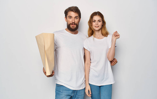 Młoda rodzina w białych t-shirtach pakiet z zakupami wycieczkę izolować tle - Zdjęcie, obraz