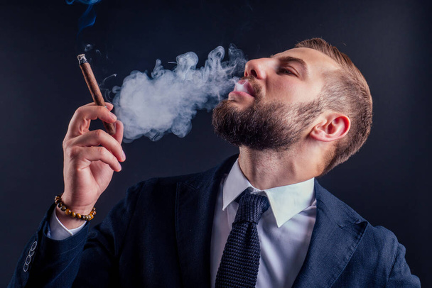 Portrait of an attractive business man with a cigar in black background studio - Photo, Image