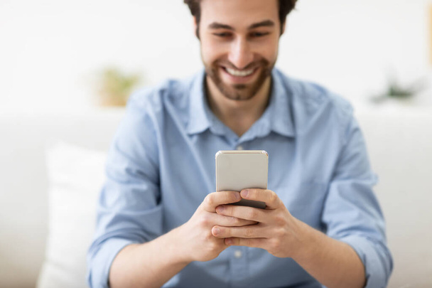 Chico feliz usando mensajes de texto para teléfonos inteligentes sentado en el sofá en casa - Foto, Imagen