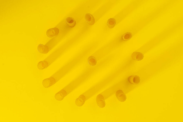 pequeño grupo de macarrones frescos rigati alineados en un círculo sobre fondo amarillo. concepto de cocina italiana - Foto, Imagen