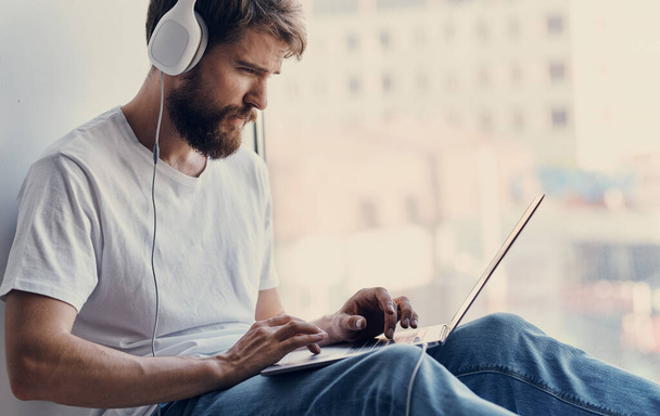 férfi laptop ül ablakpárkányon billentyűzet monitor fejhallgató modell - Fotó, kép