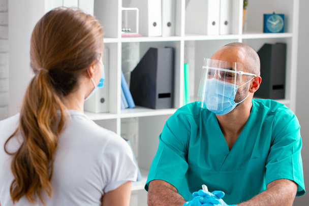 Doctor in face mask talking to female patient in clinic - Fotoğraf, Görsel