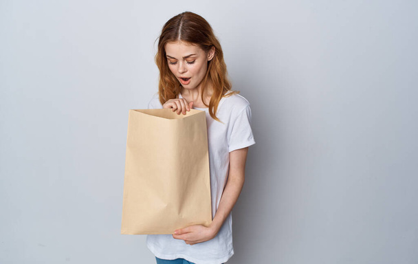 Une femme dans un T-shirt blanc et un jean avec un paquet dans ses mains avec des courses - Photo, image