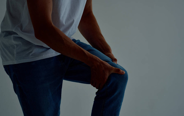 the guy touches his leg with his hands on a light background knee pain - Photo, Image