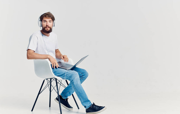 hombre en los auriculares con el ordenador portátil en sus rodillas sentado en la silla de comunicación de fondo aislado - Foto, imagen