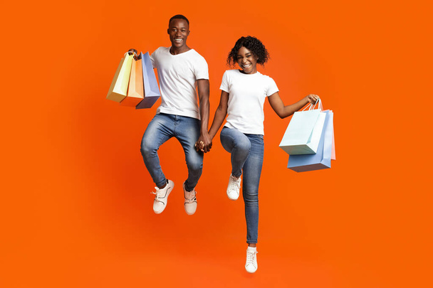 Happy black man and woman with purchases jumping up - Photo, Image