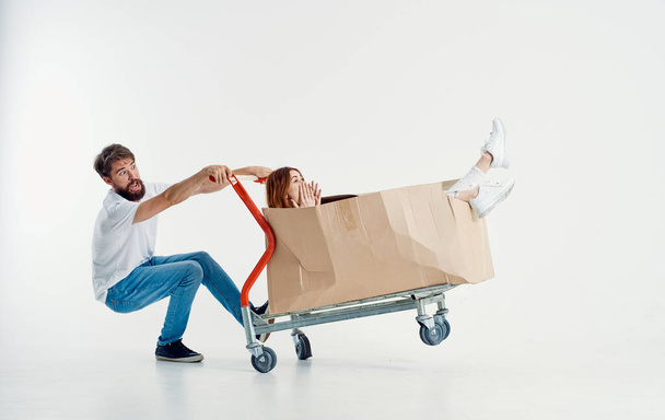 cheerful man and woman in a box on a cargo trolley emotions light background model - Photo, Image