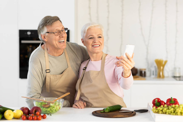 Gioioso anziani sposi making selfie having divertimento cucina in cucina - Foto, immagini