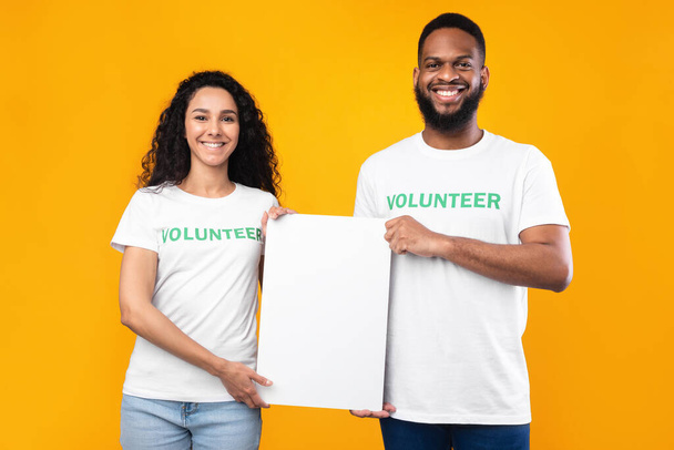 Два разных волонтера держат пустой плакат на желтом фоне - Фото, изображение