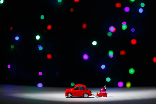 Irkuck, Rosja - 28 listopada 2020: Czerwony bożonarodzeniowy samochód wiozący sanie z piłką świąteczną w Wigilię. Szczęśliwego Nowego Roku koncepcja karty. - Zdjęcie, obraz