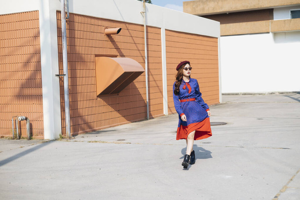 Wavy brunette woman in blue and red retro dress walking alone on rooftop. - Foto, Imagem