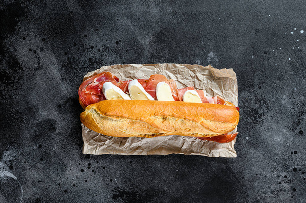bagetový sendvič s jamonovou šunkou serrano, paleta iberica, sýr Camembert. Černé pozadí, horní pohled, místo pro text. - Fotografie, Obrázek