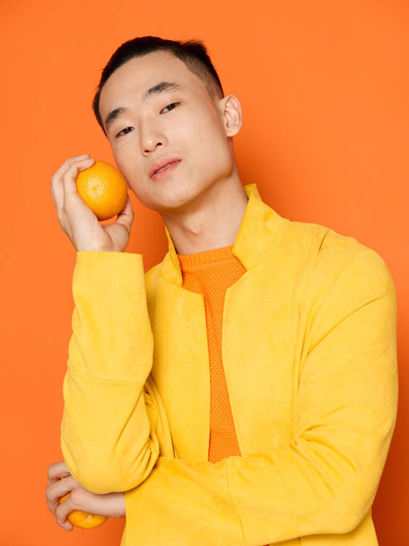 Молодий чоловік з помаранчевим в руці і жовтим піджаком ізольований фон обрізаний вид
 - Фото, зображення