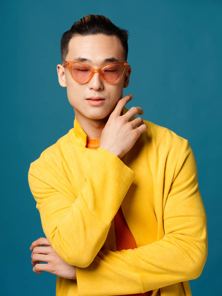 Chico de moda en gafas sobre un fondo azul y una chaqueta amarilla recortada vista del modelo - Foto, Imagen