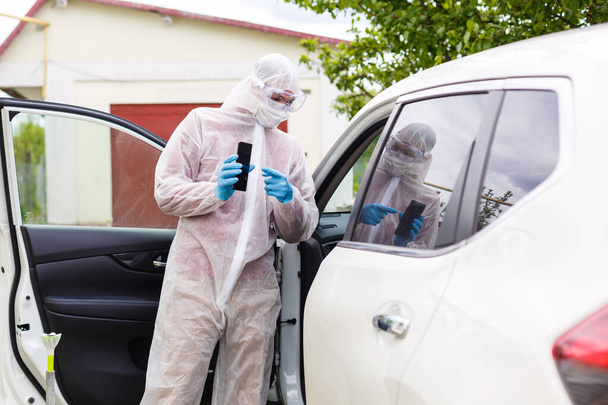 Man in protective suit, medical mask and rubber gloves for protect from bacteria and virus is driving a car. Protective mask while quarantine, world pandemic, covid 19, coronavirus, infection. - Foto, Bild