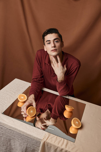 man at table with mirror and oranges top view fabric background - Foto, Imagem