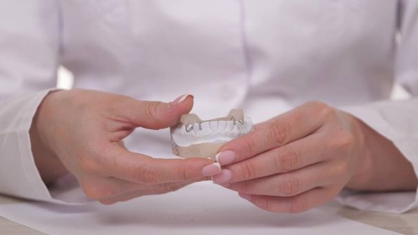 Una donna ortodontista tiene in mano una piastra per correggere denti e occlusione. Mettere il piatto sui denti bianchi intonaco. Trattamento della mandibola in uno studio medico specializzato. Un sano e bello - Foto, immagini