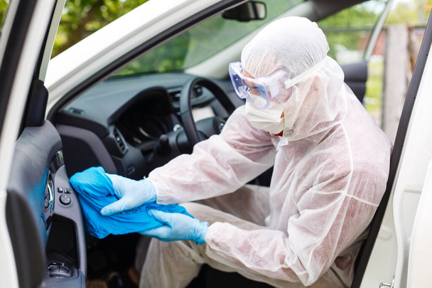 Disinfectant worker character in protective mask and suit sprays bacterial or virus in a car. - Фото, изображение
