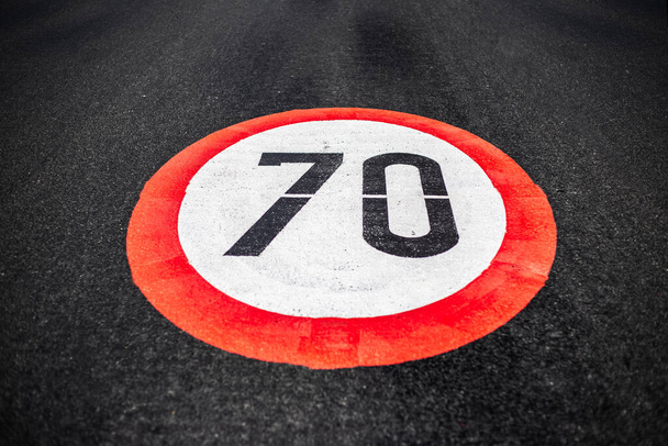70km per hour speed limit sign painted on dark asphalting road. - Photo, Image