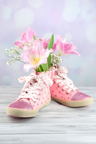 Beautiful gumshoes with flowers inside on wooden table, on light background - Zdjęcie, obraz