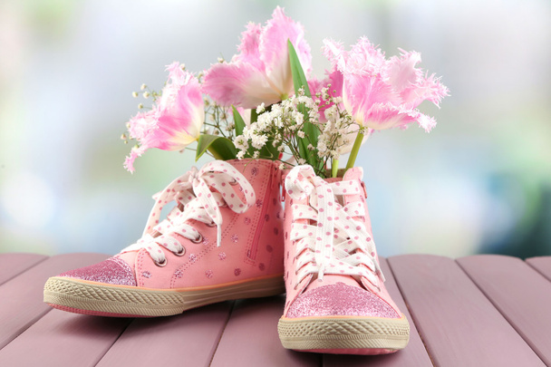 Beautiful gumshoes with flowers inside on wooden table, on light background - Фото, изображение