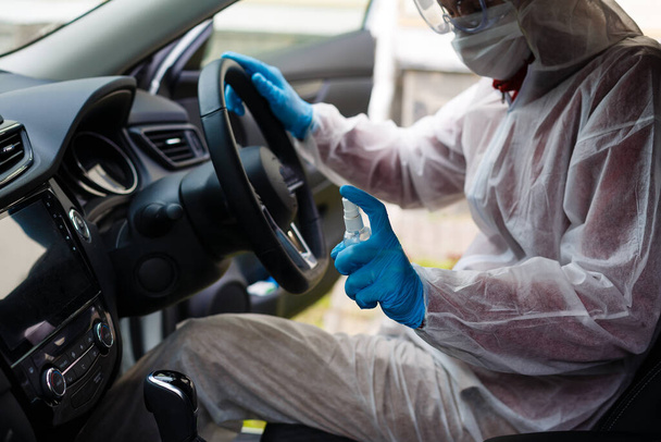 Απολυμαντικό χαρακτήρα εργαζόμενος σε προστατευτική μάσκα και σπρέι κοστούμι βακτηριακός ή ιός σε ένα αυτοκίνητο. - Φωτογραφία, εικόνα
