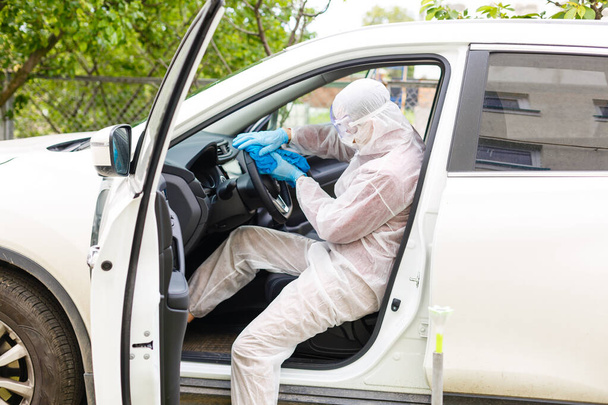 Carácter trabajador desinfectante en máscara protectora y traje pulveriza bacteriana o virus en un coche. - Foto, imagen