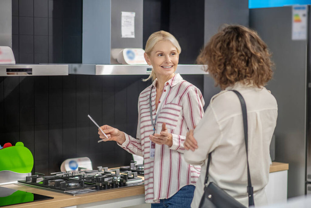 Sales assistant in striped shirt talking to female customer - Fotografie, Obrázek