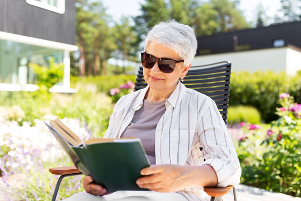 happy senior woman reading book at summer garden - 写真・画像