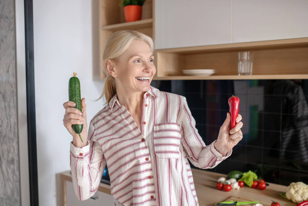 Blonde housewife holding vegetables and smiling nicely - Фото, зображення