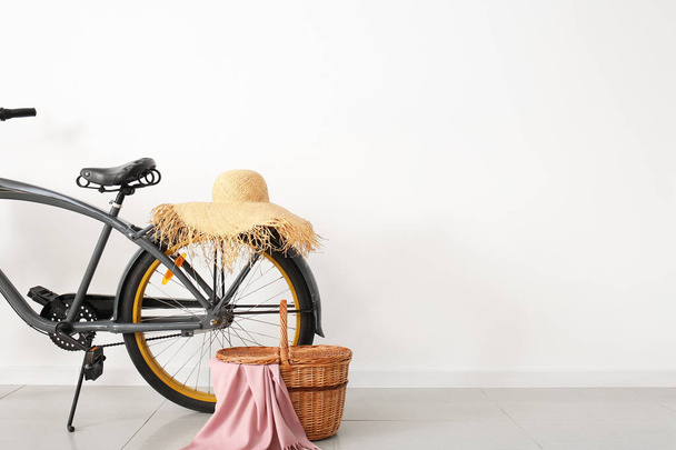 Bicicleta moderna con cesta de picnic y sombrero cerca de la pared blanca - Foto, Imagen