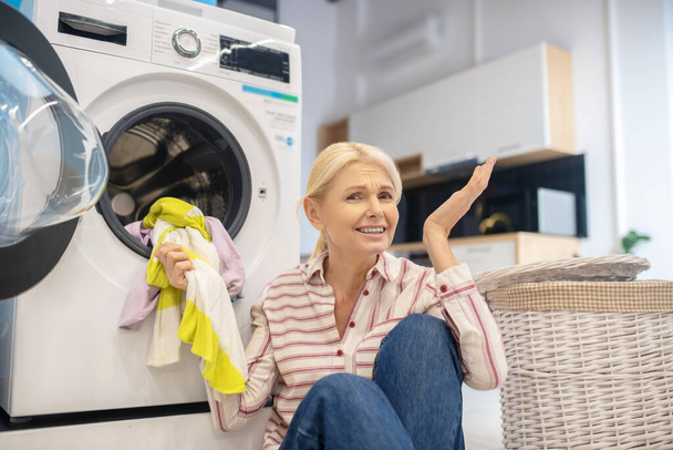 Blonde housewife in striped shirt sitting near the washing machine - 写真・画像