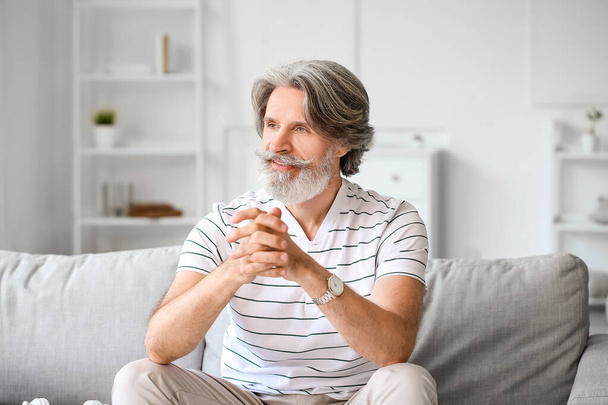 Homem maduro com cabelos grisalhos sentado no sofá em casa - Foto, Imagem