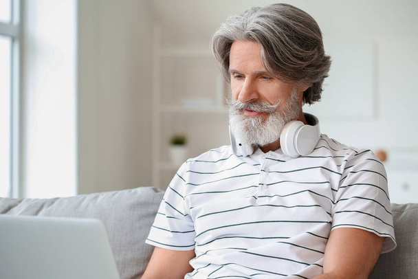 Homem maduro com fones de ouvido e laptop em casa - Foto, Imagem
