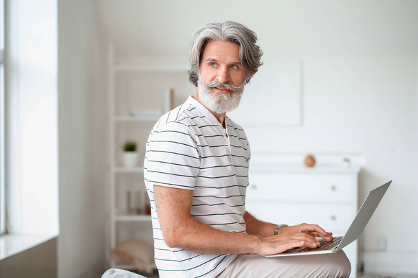 Felnőtt férfi laptoppal ül a kanapén otthon - Fotó, kép