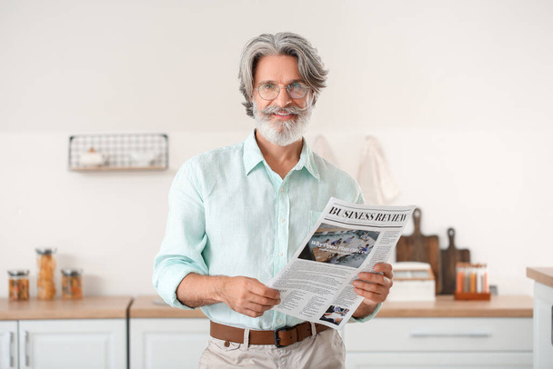 Старший мужчина с газетой на кухне - Фото, изображение