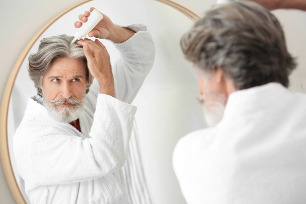 Volwassen man met serum voor haaruitval behandeling in de buurt van spiegel - Foto, afbeelding
