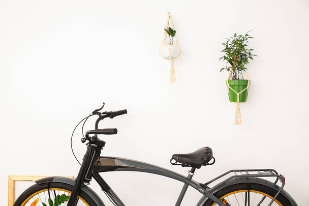 Modern bicycle with houseplants near white wall - 写真・画像