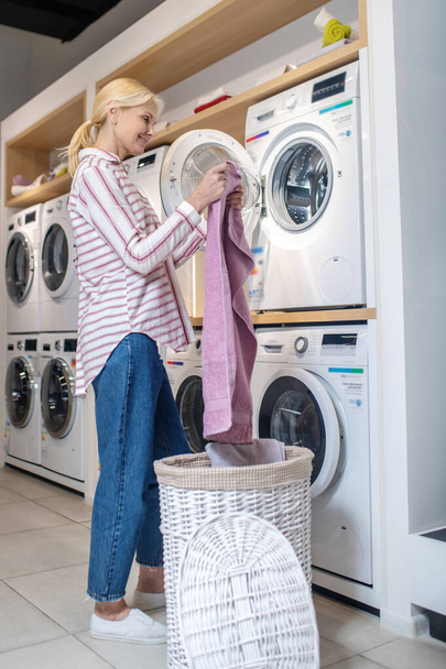 Blonde woman in striped shirt taking clothes out of basket - Photo, image