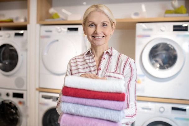 Femme blonde souriante tenant une pile de serviettes - Photo, image