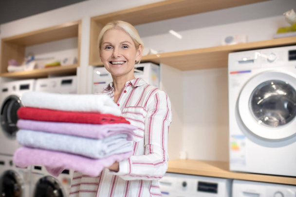 Smiling blonde woman holding a pile of towels and feeling good - Foto, Bild