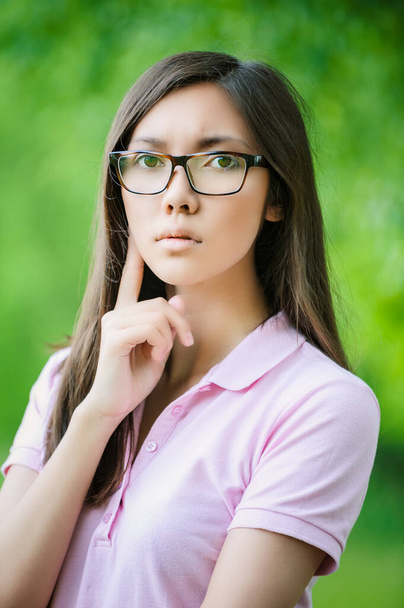 緑豊かな夏の公園の背景にピンクのブラウスと眼鏡で若い浸透美しいアジアの女性. - 写真・画像