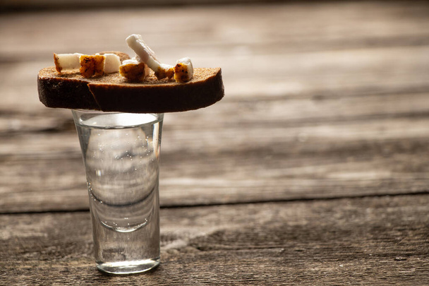 un vaso de vodka junto a un pedazo de pan negro con tocino en una mesa de madera en la cocina para el almuerzo en ucraniano - Foto, Imagen